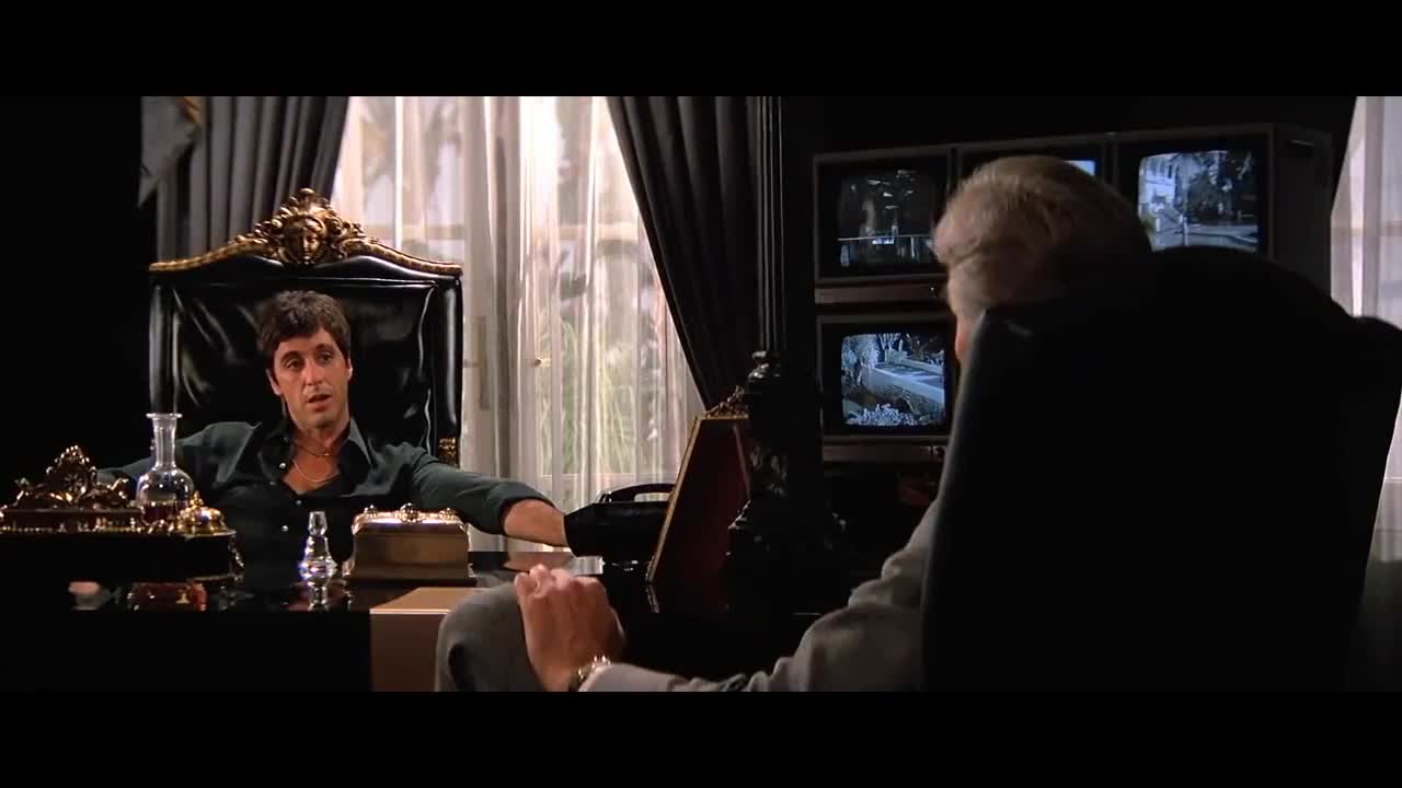 Imagen de una escena emblemática de scarface en la que Tony Montana trajeado y drogado fuma un puro mientras discute sobre sus varias actividades económicas que no son compliant.