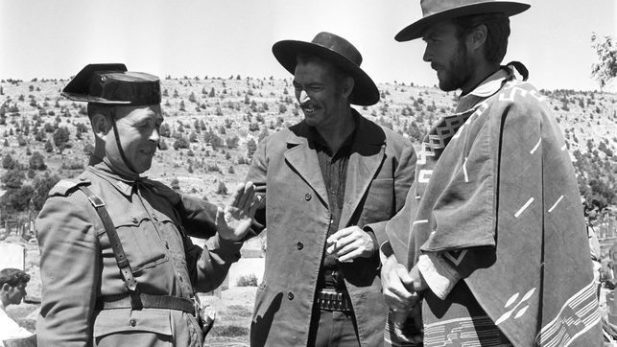 Una foto en blanco y negro de un guardia civil hablando con dos hombres en medio del campo.